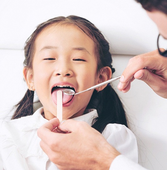 A dentist uses dental instruments to perform an oral cancer screening on a little girl