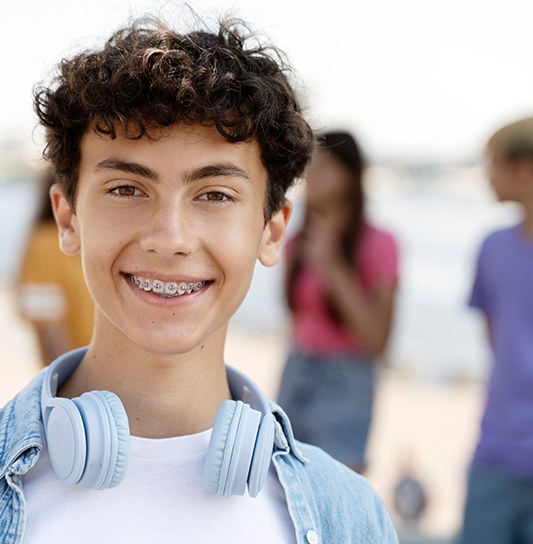 Boy in denim shirt with blue headphones smiling with braces outside with friends