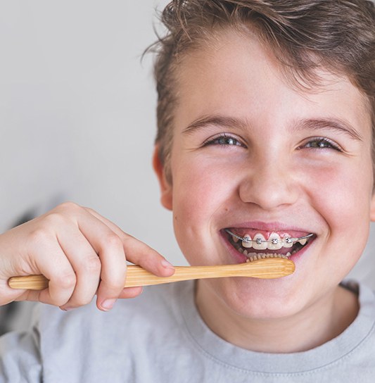 Boy in gray t-shirt brushing braces with a wooden toothbrush