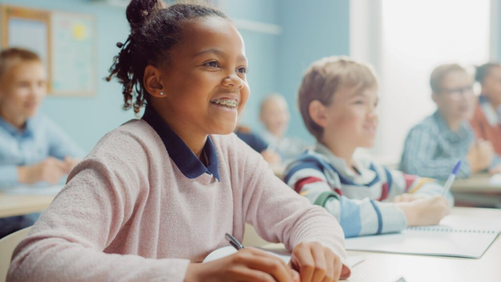 Little girl in pink sweater smiling at school with classmates